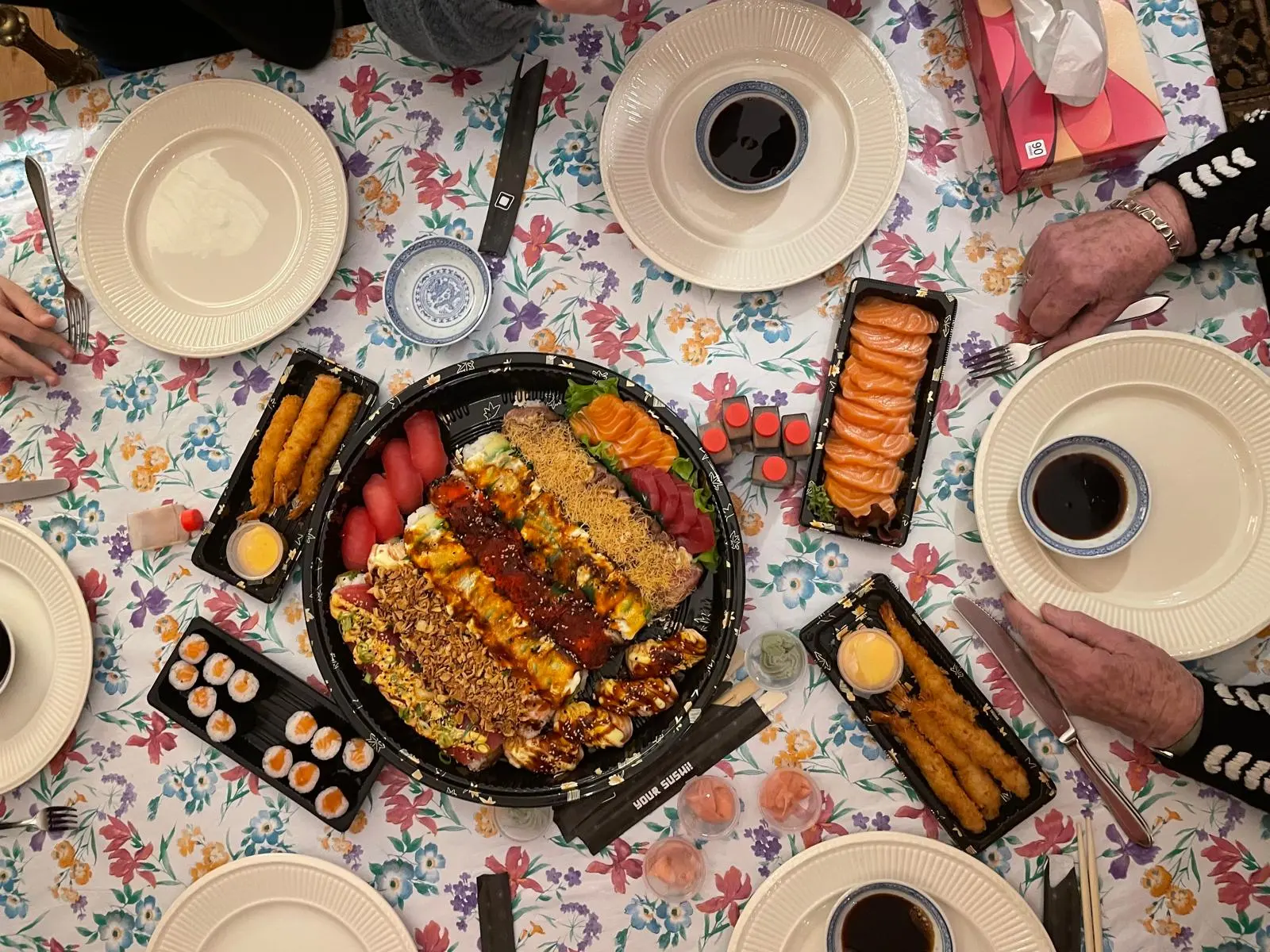 Een tafel van bovenaf met een grote sushischaal en bakjes zalm tussen de borden